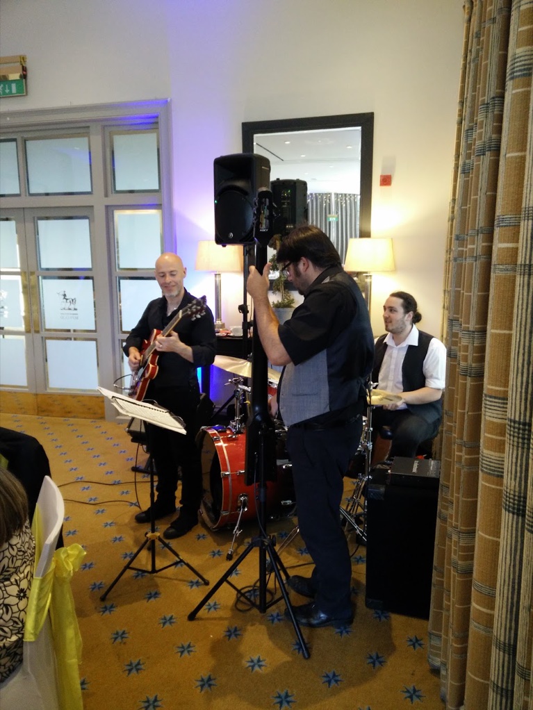 Guitar, upright bass and drums playing in a corner of the room at Bowood during the wedding breakfast